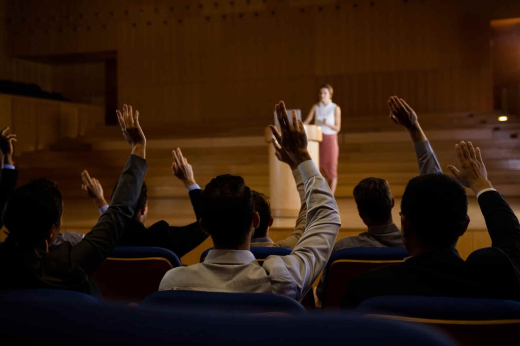 audience raising their hands and female keynote speaker on stage
